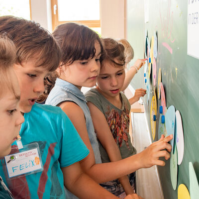 Grundschulkinder arbeiten in Gruppen an einer Tafel und setzen sich spielerisch mit zentralen Inhalten des Pr&auml;ventionsprogramms &raquo;Unsere verr&uuml;ckten Familien&laquo; auseinander.