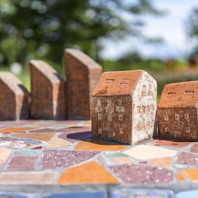 F&uuml;nf Ziegel in Form von H&auml;usern stehen auf einem bunten Mosaikfeld.