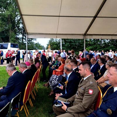 M&auml;nner in Uniformen und Anz&uuml;gen sitzen in Stuhlreihen auf einer Festwiese unter einem Festzelt.