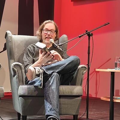 Der Autor Sven Stricker sitzt in einem Sessel auf der B&uuml;hne und liest aus seinem neusten Buch.
