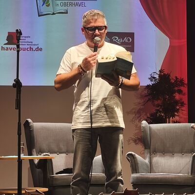 Der Autor Andreas Winkelmann steht auf der B&uuml;hne und liest aus seinem humorvollen Campingkrimi "Entf&uuml;hrung im Himmelreich".