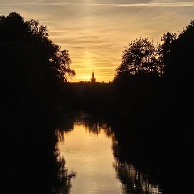 Ein See liegt in der Abendd&auml;mmerung, im Hintergrund ist der Umriss eines Hauses zu sehen.