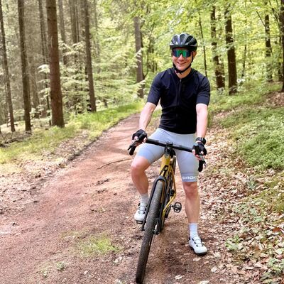 Ein Mann in Fahrradbekleidung steht mit seinem Rad im Wald.
