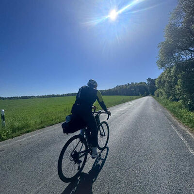 Ein Radfahrer f&auml;hrt im Sonnenschein auf einer Stra&szlig;e an einem Feld.